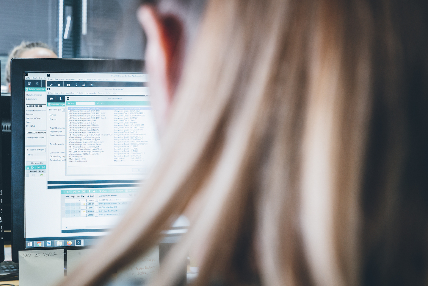Person vor einem Computerbildschirm mit geöffneter Benutzeroberfläche und Tabellenansicht.